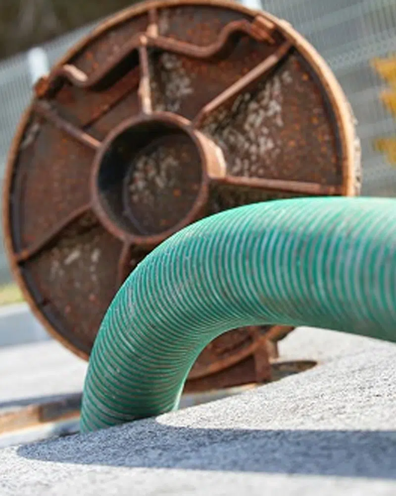 Green vacuum hose curving over pavement beside a rusted tank lid — Si View Septic Pumping in North Bend