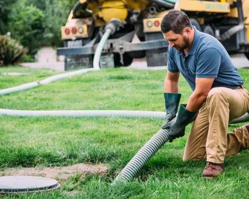 Technician kneeling on lawn handling septic vacuum hose near tank lid — Si View Septic Pumping in North Bend